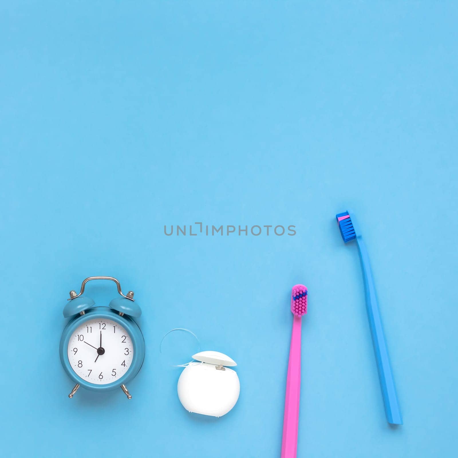 Teeth hygiene and oral dental care products and alarm clock on blue color background with copy space. Two family toothbrushes. Flat lay, top view composition, mockup. Morning routine concept