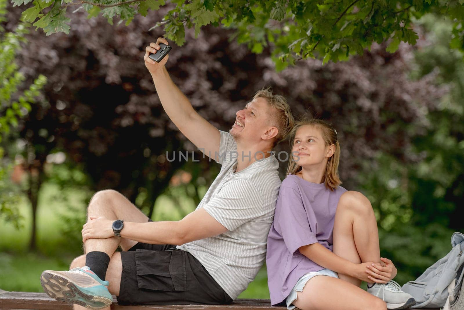 Father And Daughter Taking A Selfie On A Summer Bench, Enjoying Family Time Together