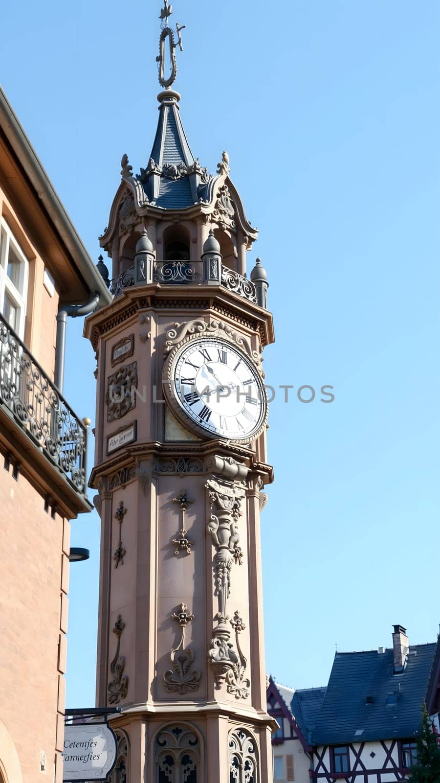 A beautifully ornate clock tower stands in a quaint street, showcasing intricate designs and a prominent clock face, surrounded by charming medieval buildings on a sunny day.