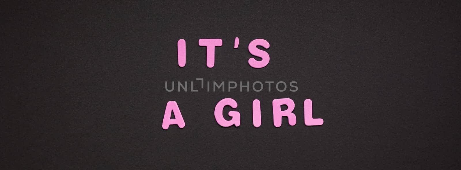 Creative pink text made from plastic letters It's a girl writing on black paper background with copy space. Baby shower concept, celebration card template