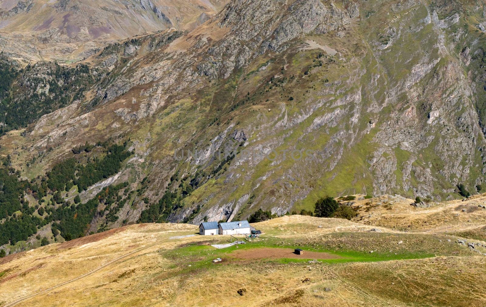 A small house sits on a hillside with a view of the mountains. The house is surrounded by a lush green field. The scene is peaceful and serene