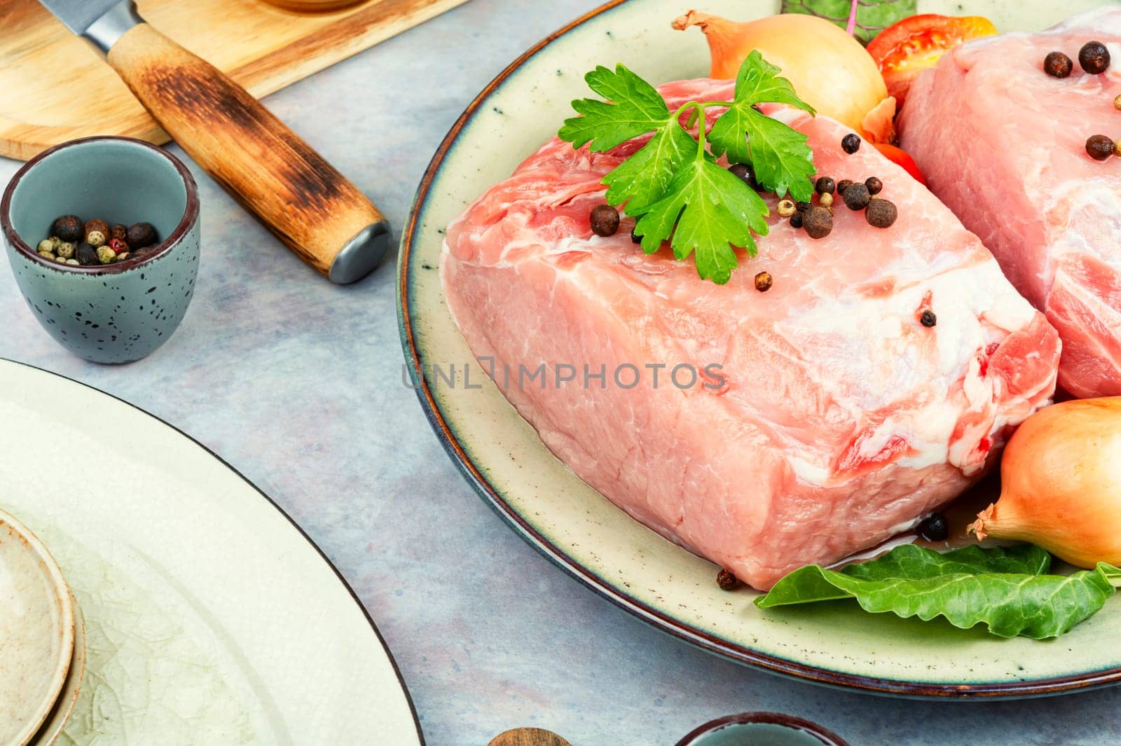 Slices of raw pork meat and vegetables on rustic wooden background.