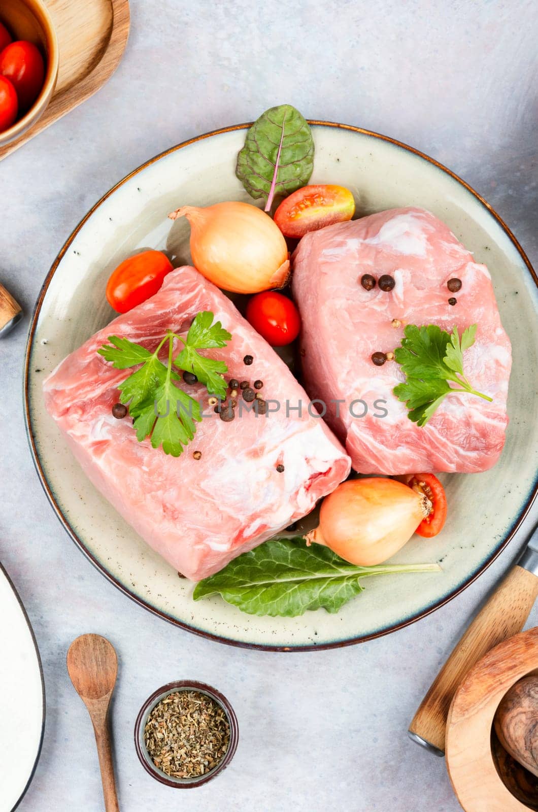 Slices of raw pork meat and vegetables on rustic wooden background.
