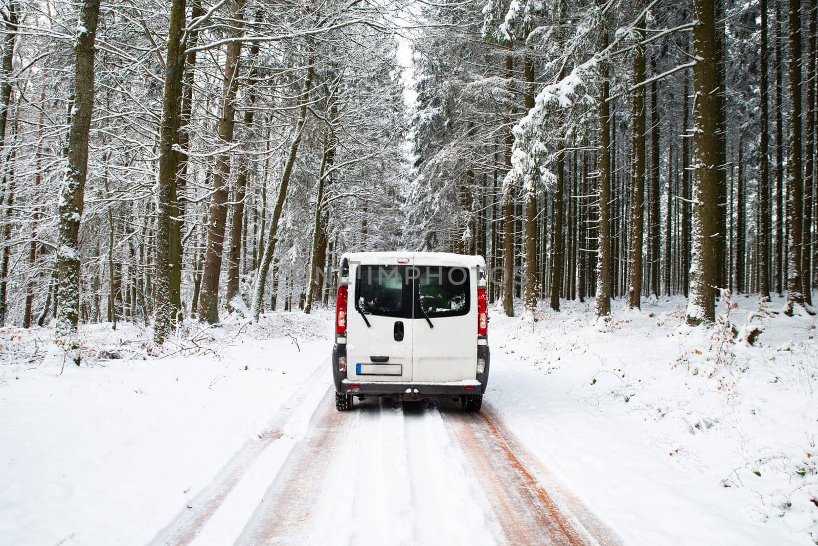 Camper Van driving on a road through a snow covered forest in winter, adventure vacation and lifestyle in the woodlands, slippery highway