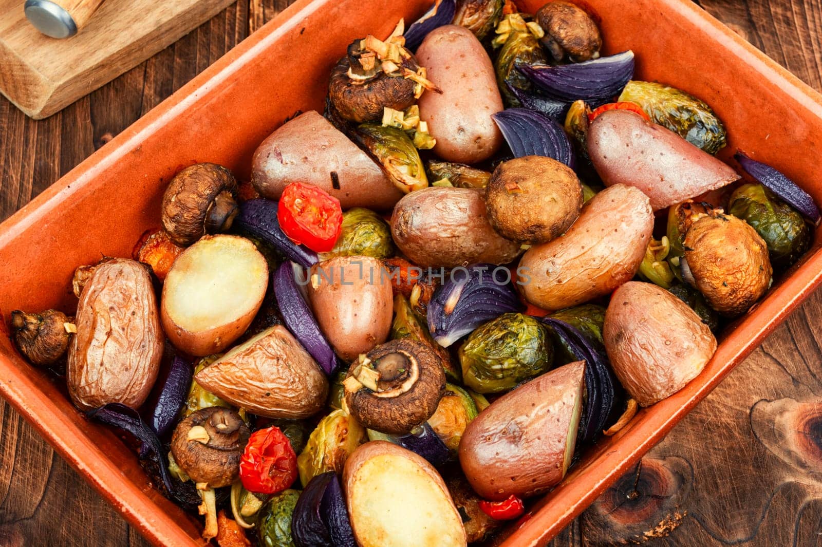 Roasted baked mushrooms, Brussels sprouts, and potatoes, garnished with onion in the oven dish. Free space for your text.