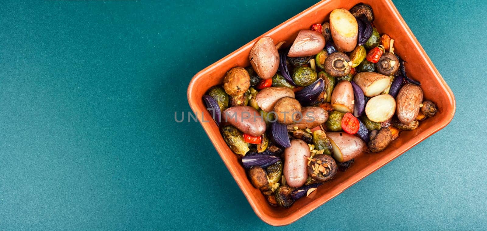 Roasted baked mushrooms, Brussels sprouts, and potatoes, garnished with onion in the oven dish. Free space for your text.