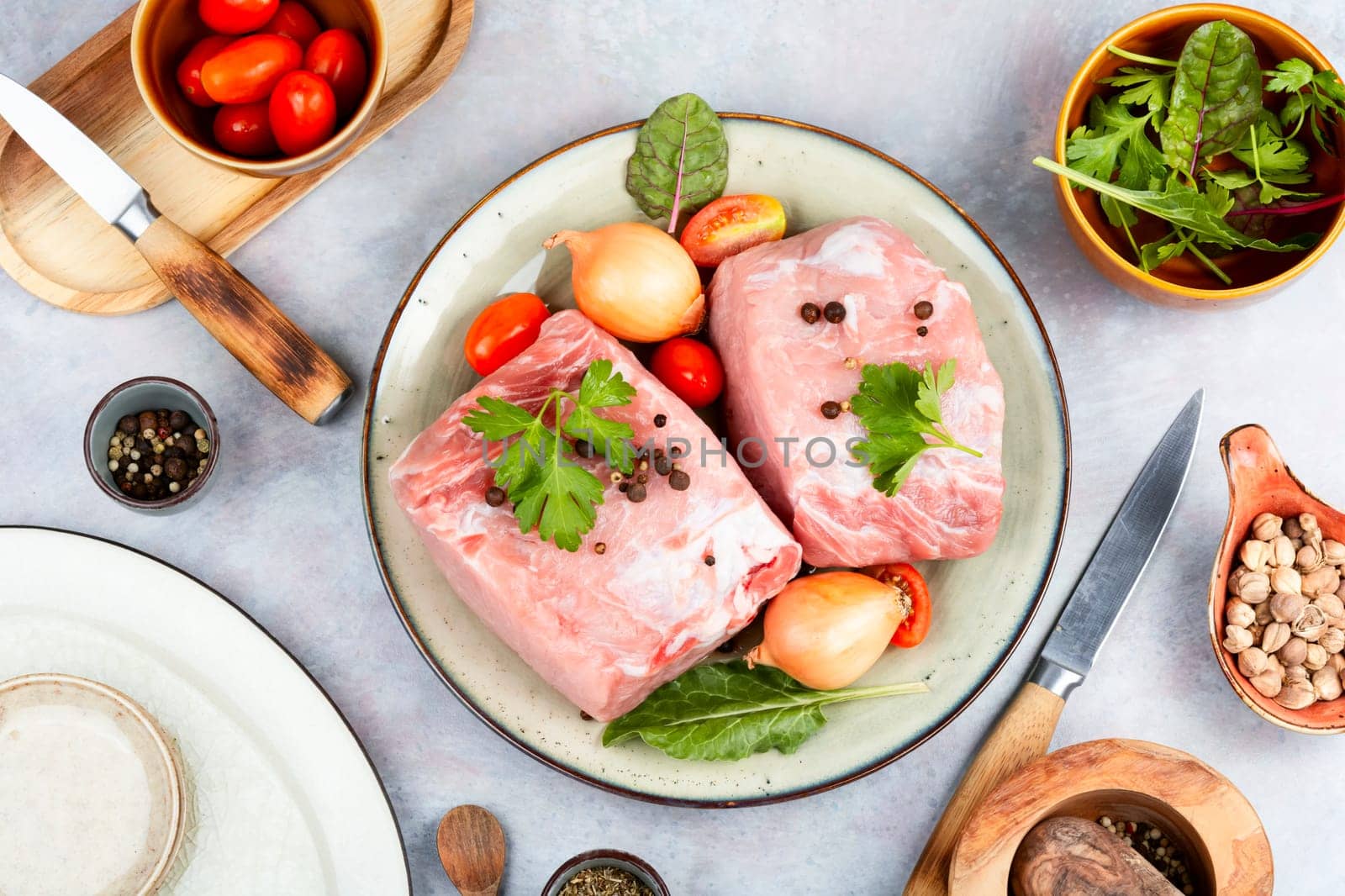 Plate with two pieces of raw meat and fresh vegetables for cooking.