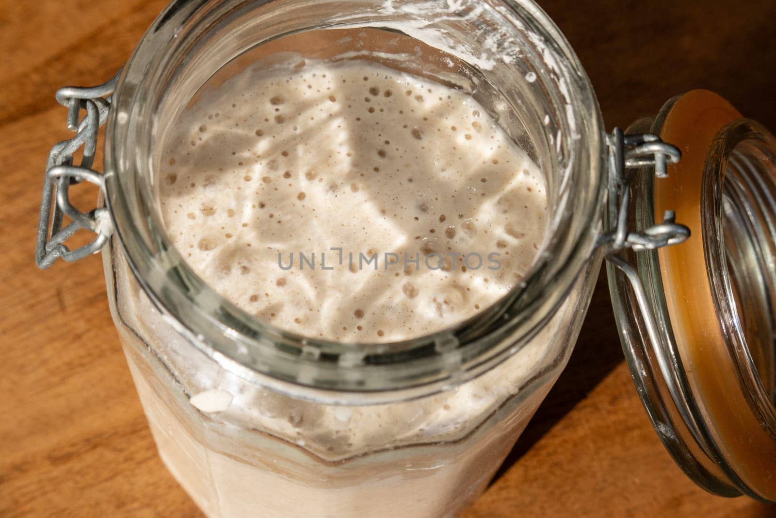 Sourdough starter or leaven, living yeast rising and bubbling in a clear glass storage jar