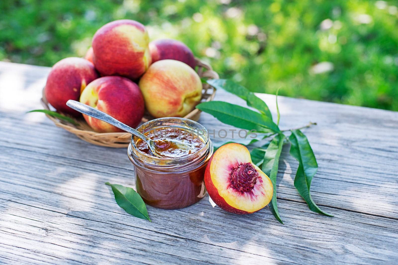 Peach jam or marmalade in a glass jar with ripe peaches, outdoors on sunny day