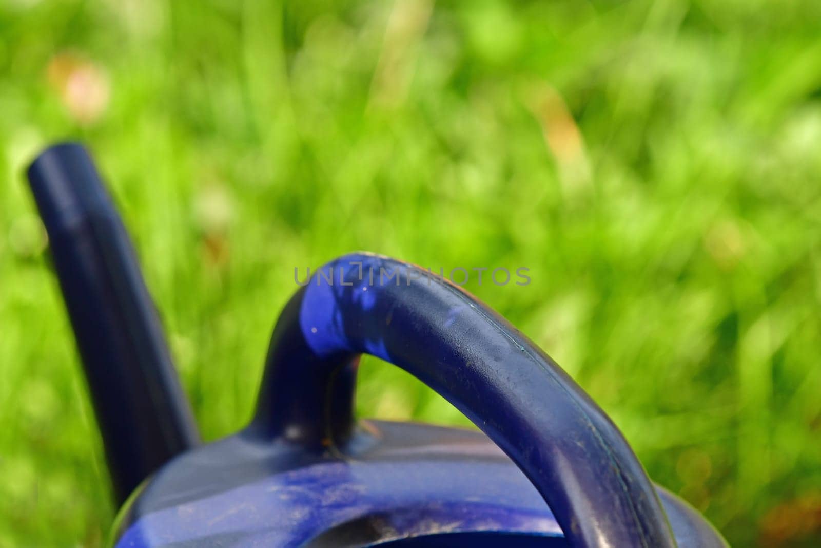 blue watering can in a garden with green blurred empty background