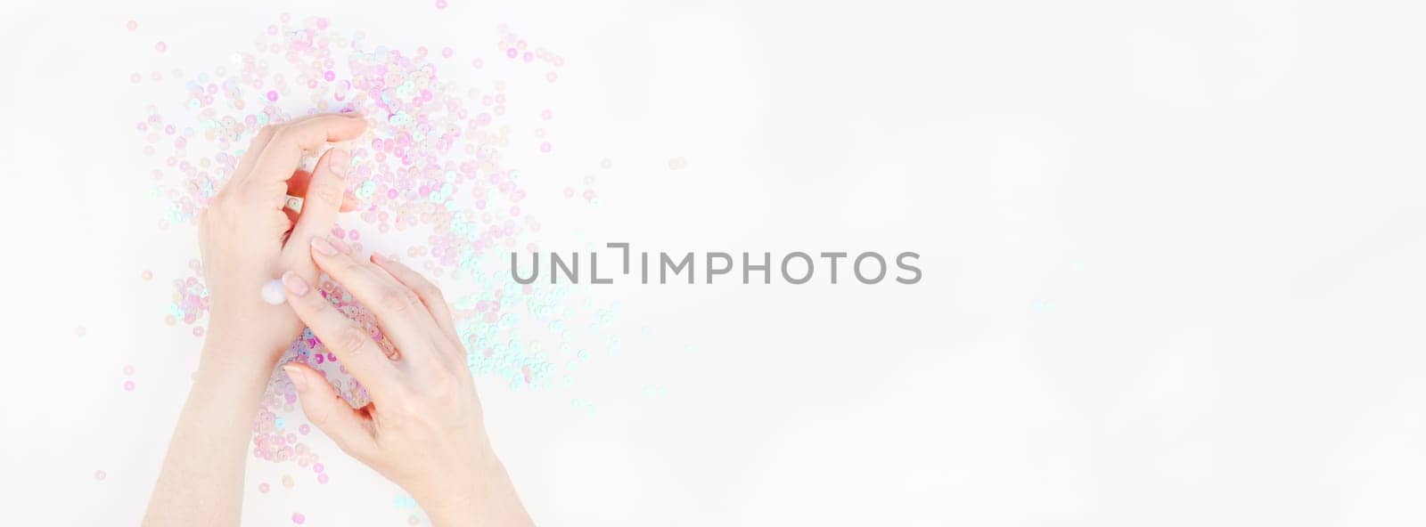 Woman moisturizing her hands with cosmetic cream lotion white pearl pastel confetti sparkles background with copy space. Creative conceptual top view flat lay backdrop for your beauty blog text design