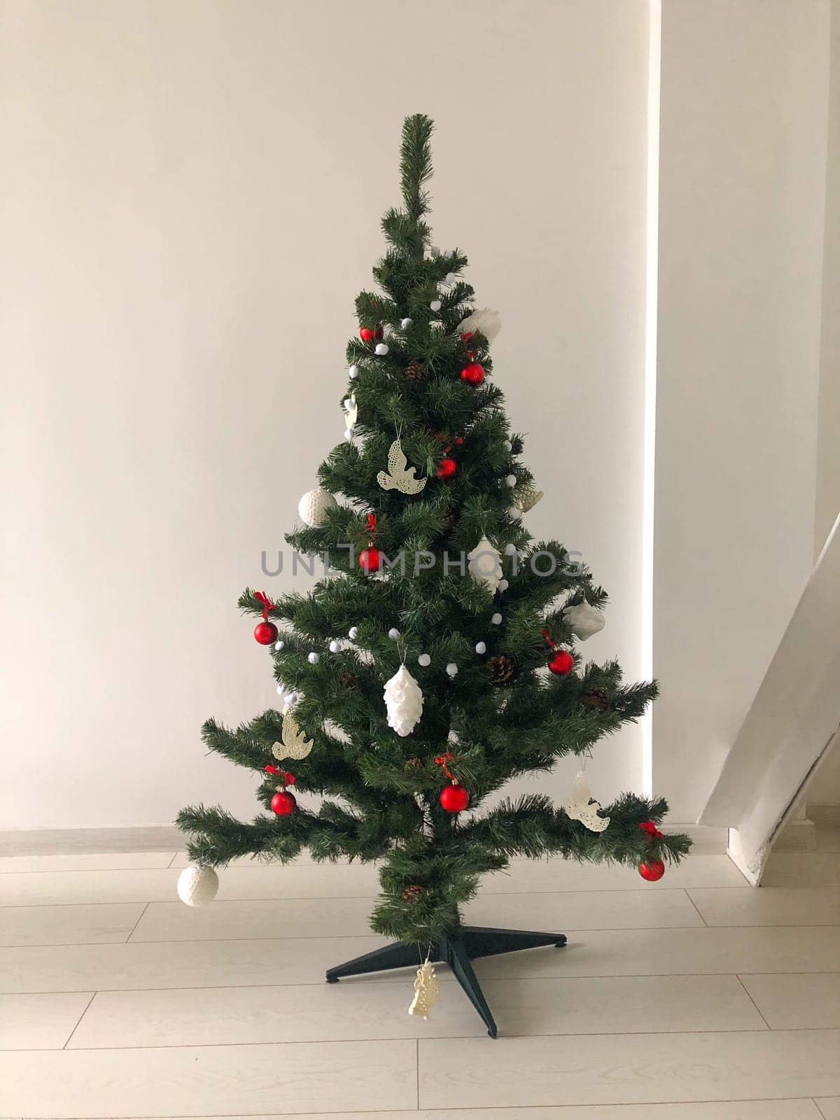 A minimalist Christmas tree decorating a modern living space, adorned with red, white, and silver ornaments. Simplicity design and festive charm to the clean, contemporary room. Minimalistic xmas decor concept.