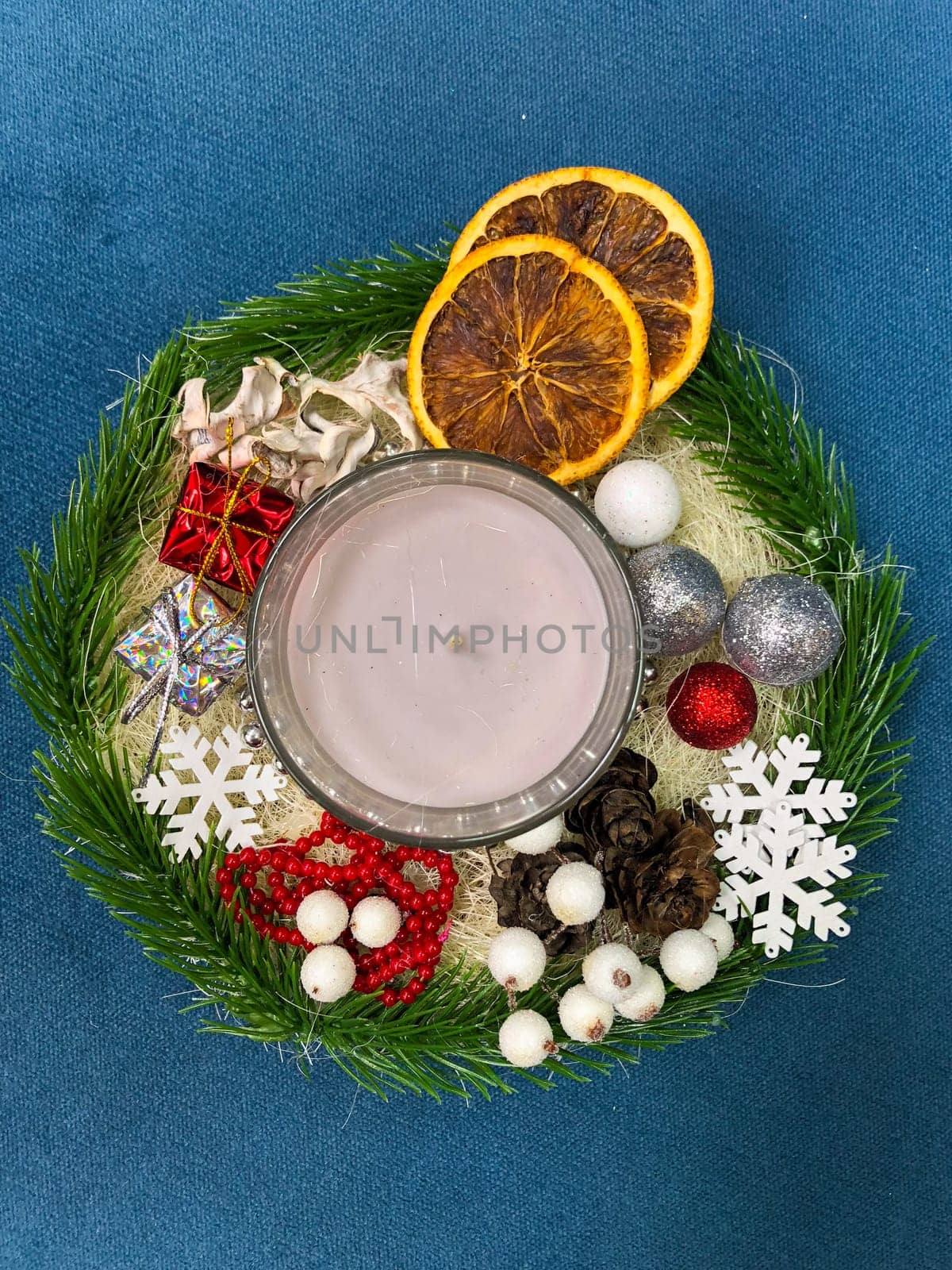 festive Christmas arrangement featuring a lit candle, dried oranges, ornaments, and holiday decorations on a blue background. holiday season and warm inviting atmosphere. Celebration and xmas decoration concept