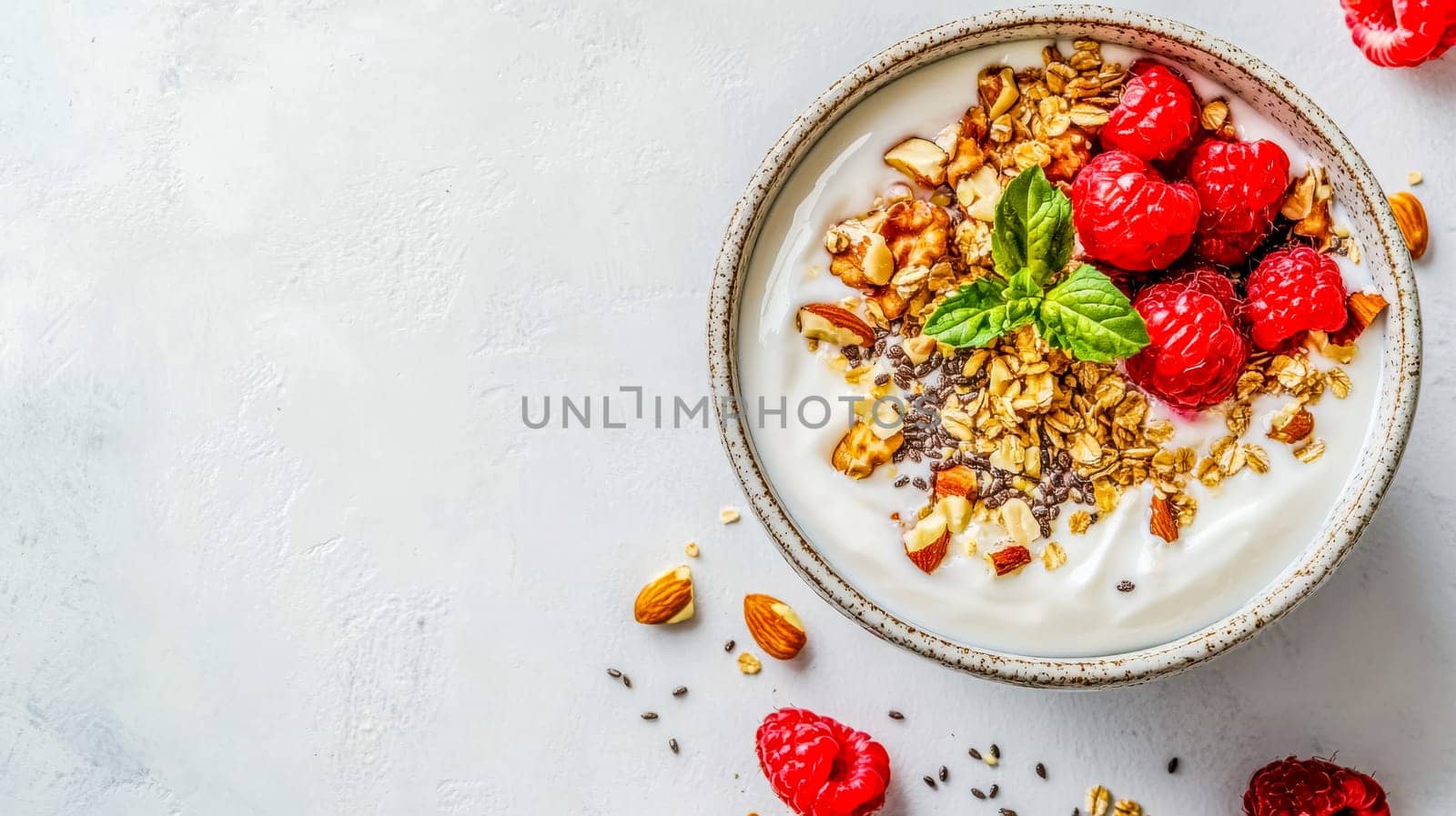 Bowl of yogurt is topped with fresh raspberries, granola, almonds, walnuts, and chia seeds, making for a healthy and delicious breakfast option