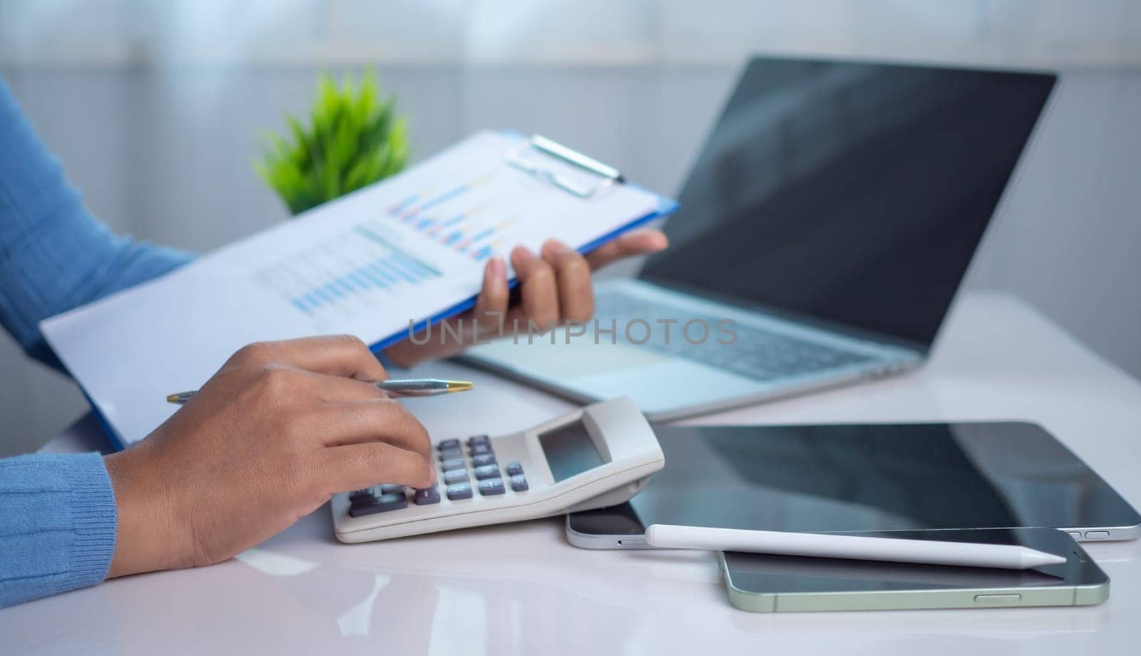 Businesswoman hand working with finances about cost and calculator and laptop with tablet on desk at office in morning light, Business accounting concept, Calculating or checking balance.