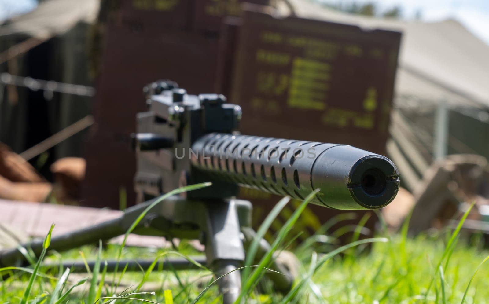 A machine gun on it is sitting on a grassy field. The gun is surrounded by a tent and a box