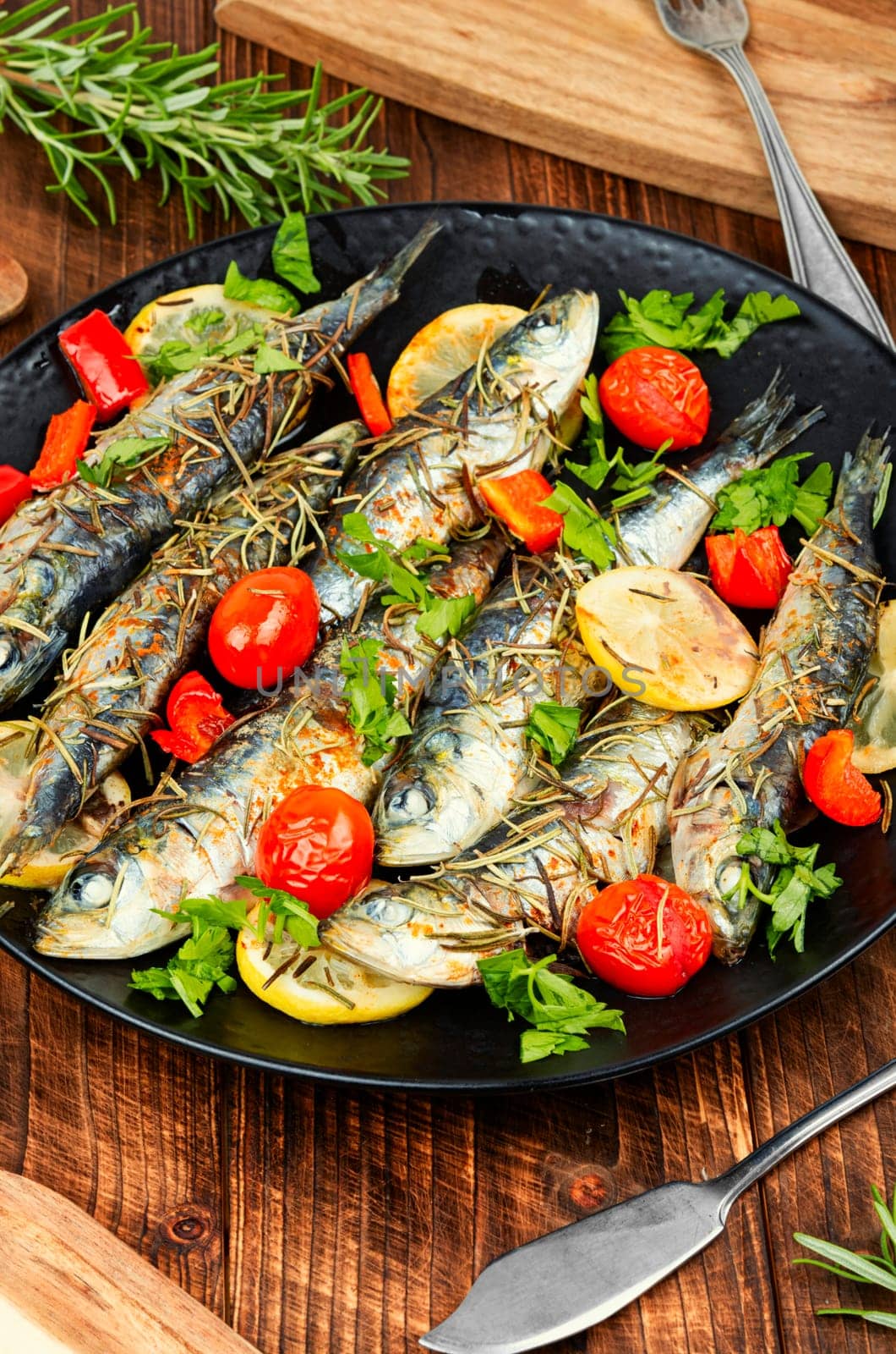 Oven baked italian fish sardoncini or sardines, with tomatoes, lemon and rosemary.