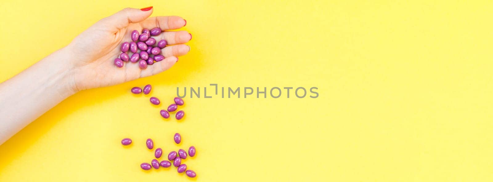 Woman hand holding purple pills handful isolated on bold yellow background with copy space. Template for feminine beauty blog social media. Female healthcare or suicide prevention concept