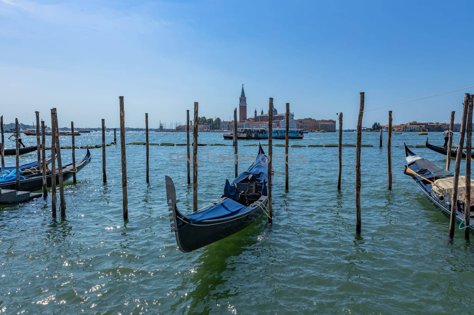 Venice, Italy - July 26, 2024: Gondolas against the San Giorgio island in Venice, Italy. Gondola is the most attractive tourist transport in Venice. Traveling and vacation in sunny Venice.