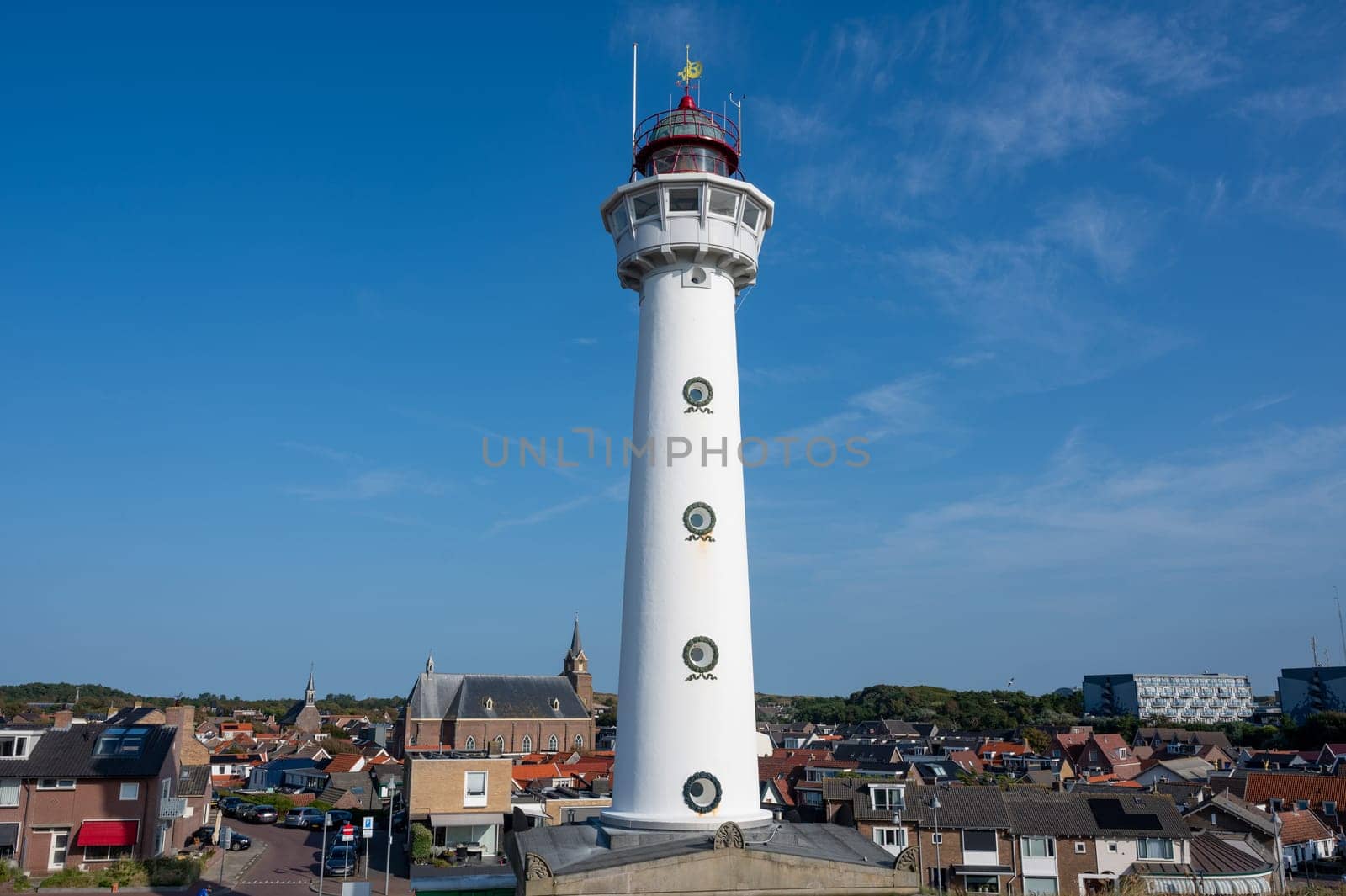 The approx. 28 m high white lighthouse J.C.J. van Speijk in Egmond aan Zee, North Holland, Netherlands with some of the town's houses