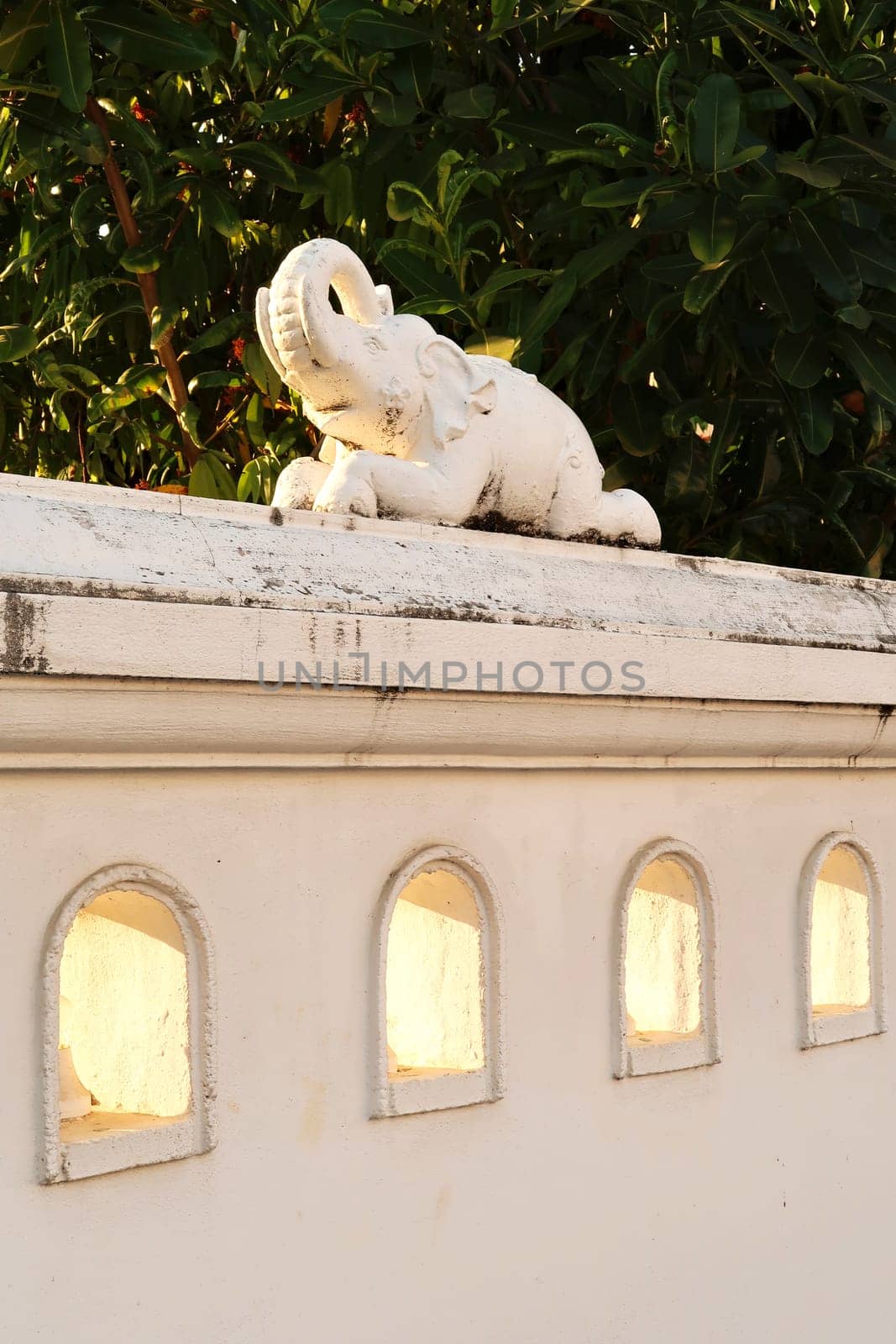 Small decorative elephant sculpture, figurine, statue on a white wall next to a park at golden hour, Chiang Mai, Thailand 2023