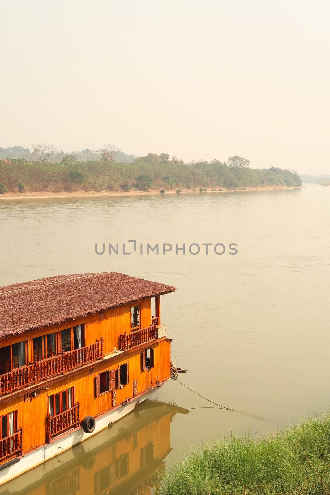 View over the Mekong River with a passenger boat, ship for a Mekong River Cruise docked at the shore in the foreground, Wiang Chiang Kong, Thailand 2023