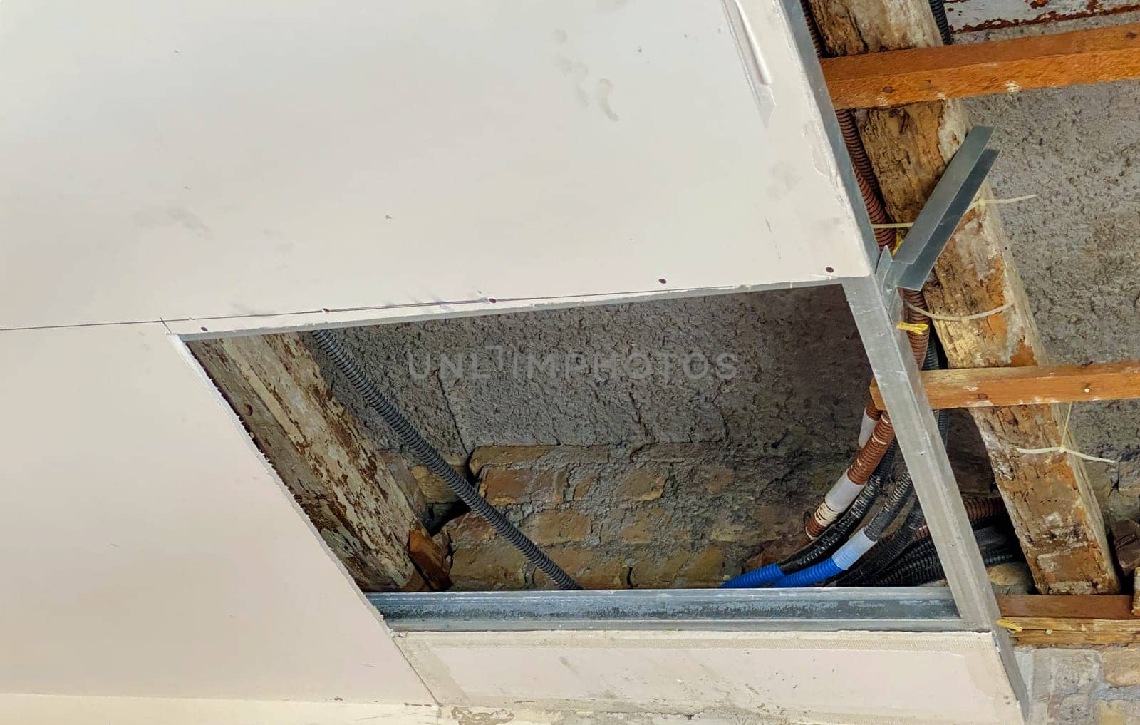An indoor view of a ceiling under restoration, showing exposed electrical wiring, insulation materials, and a partially removed plasterboard panel.