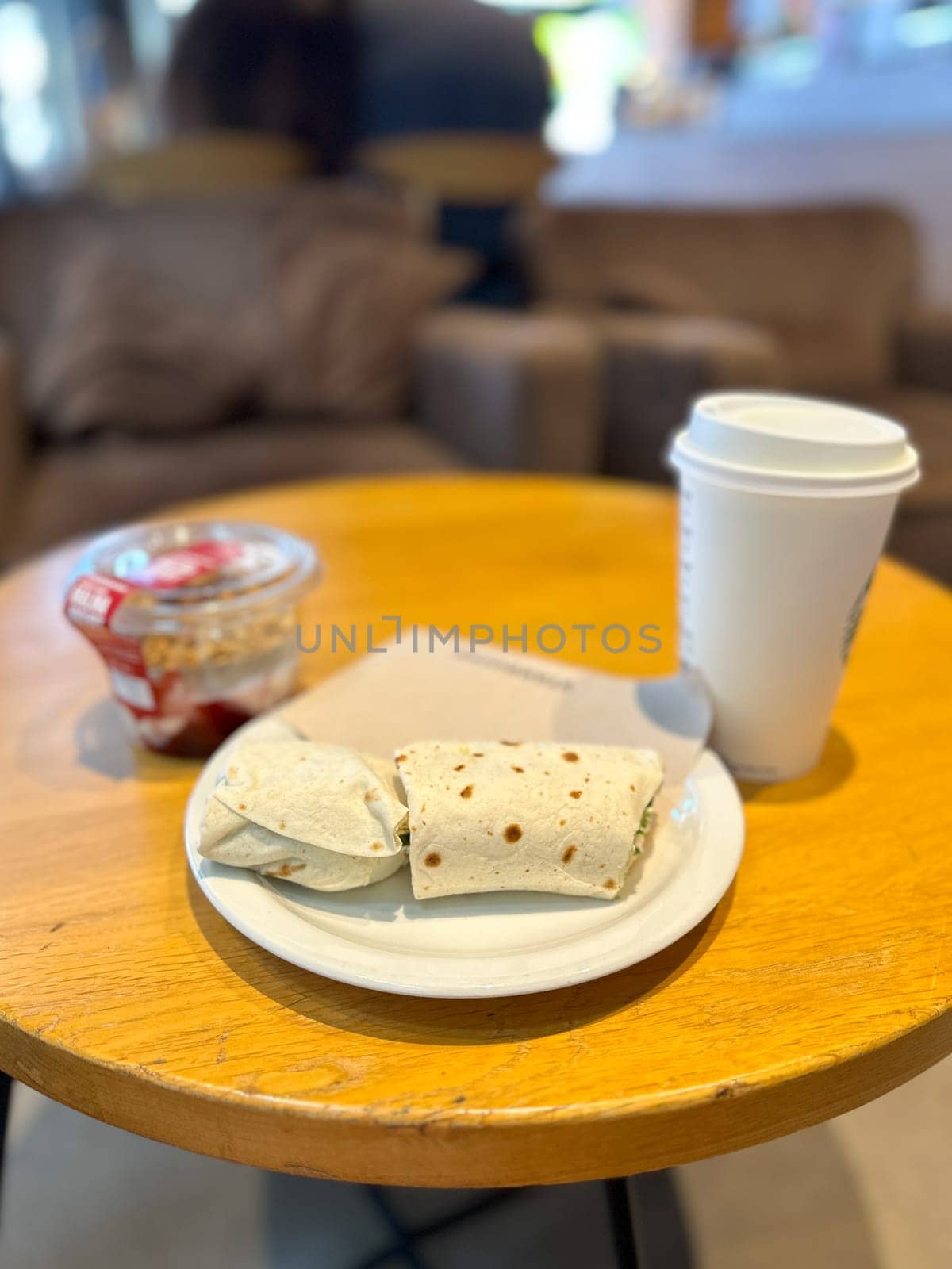 Delicious breakfast on a wooden table in a cozy coffee shop. Wrap, yogurt with muesli and coffee. Comfort and relaxation and starting the day with a taste food concept.