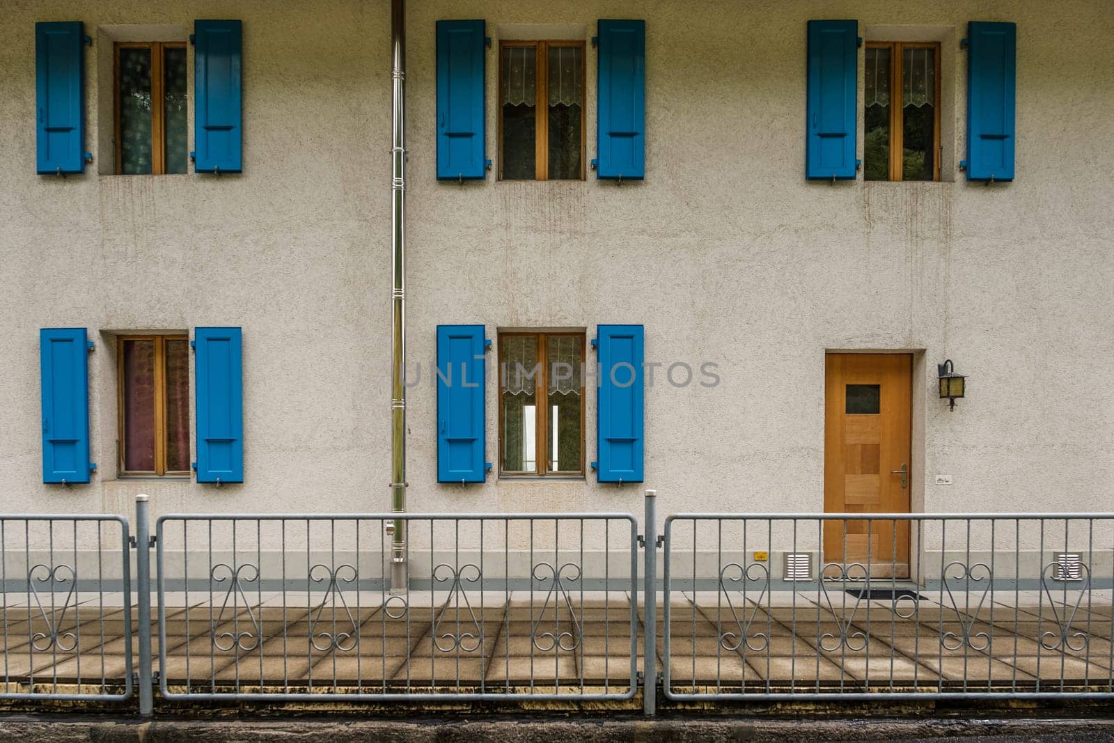 Exterior of a building with five windows with open blue shutters and a brown front door