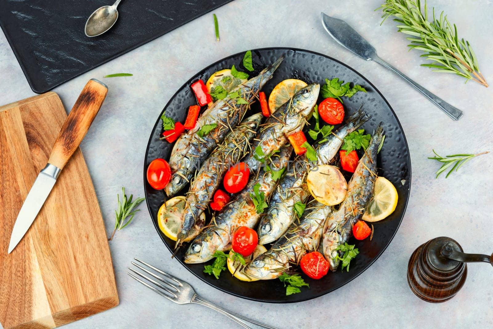 Baked sardine fish with lemon, cherry tomatoes and rosemary on ceramic plate on rustic wooden table. Healthy and tasty dinner. Copy space.