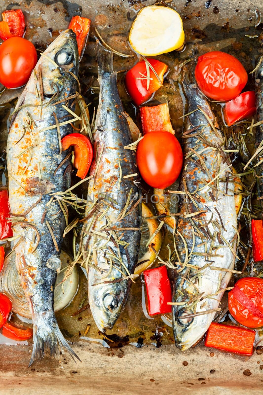 Baked sardine fish with lemon, cherry tomatoes and rosemary on ceramic plate on rustic wooden table. Healthy and tasty dinner. Copy space.