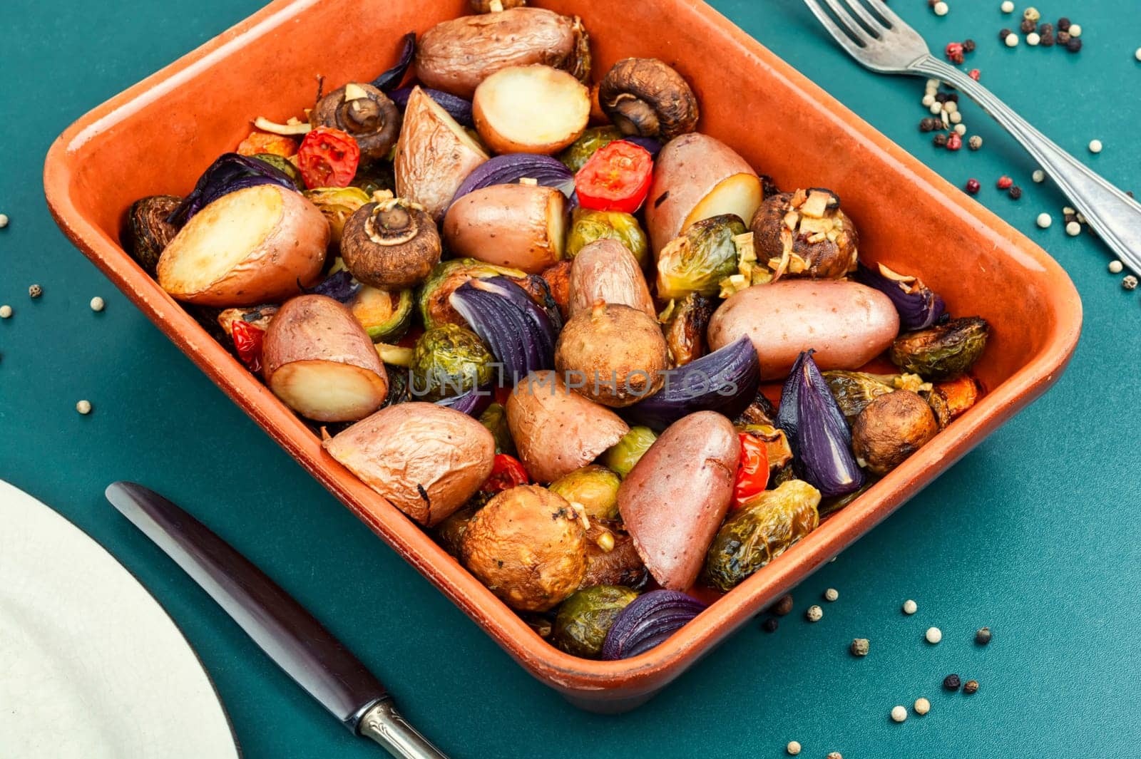 Autumn roasted vegetables. Stewed mushrooms, Brussels sprouts, and potatoes, garnished with onion on a baking dish.