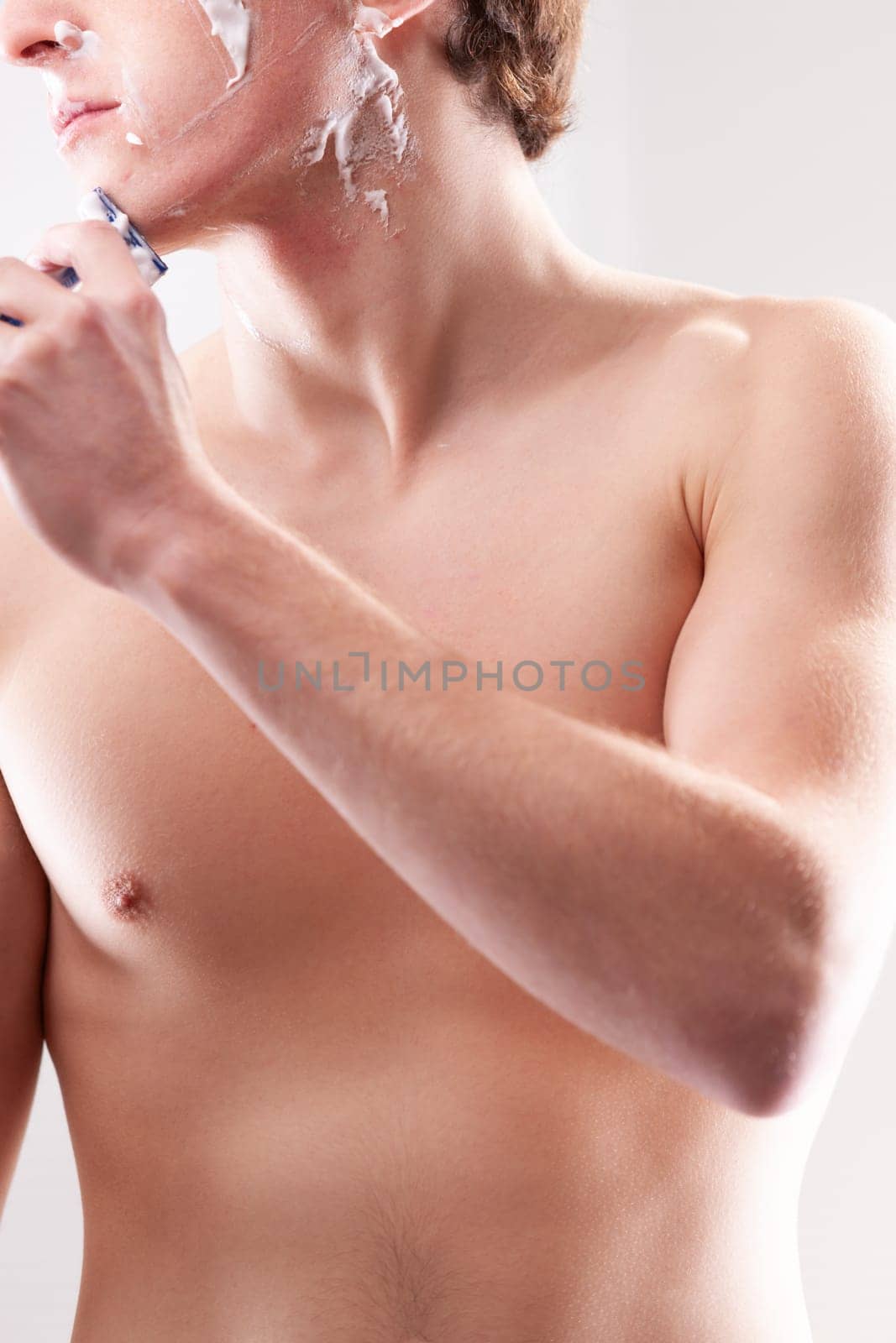 Young man carefully shaving his face with a razor in the bathroom, creating foam for a smooth shave and feeling fresh and confident