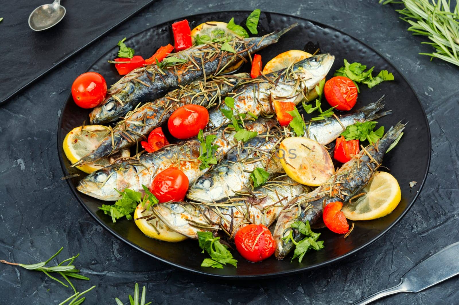 Sardines roasted with cherry tomatoes rosemary and lemon on table.