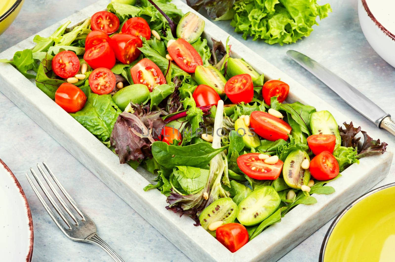 Juicy salad with cherry tomatoes and fresh lettuce leaves on a modern stone tray. Space for text.