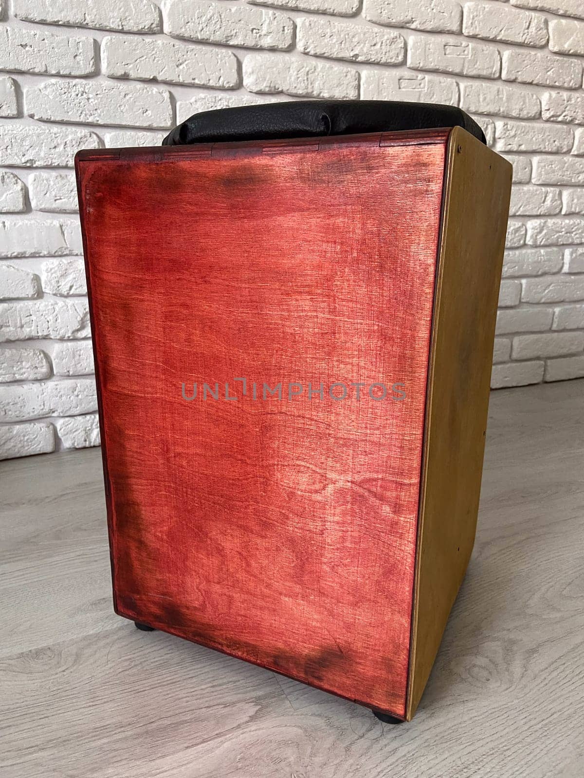 Cajon drum sits elegantly against a textured white brick wall, highlighting its wooden craftsmanship. Musical Instrument for creating music at home and hobby concept.