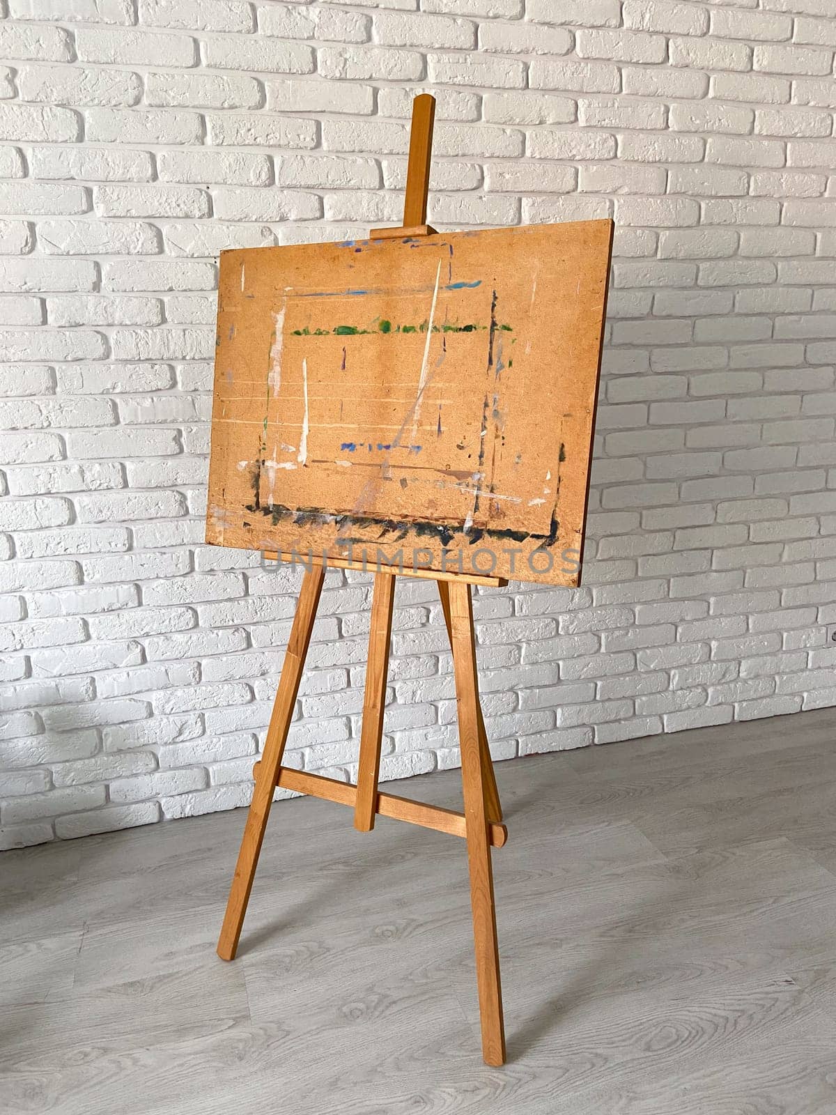 An artist's easel stands elegantly against a textured white brick wall, with well-used wooden canvas holder. Creativity and artistic expression concept.