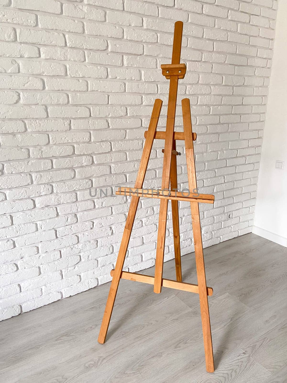An artist's easel stands elegantly against a textured white brick wall, with well-used wooden canvas holder. Creativity and artistic expression concept.