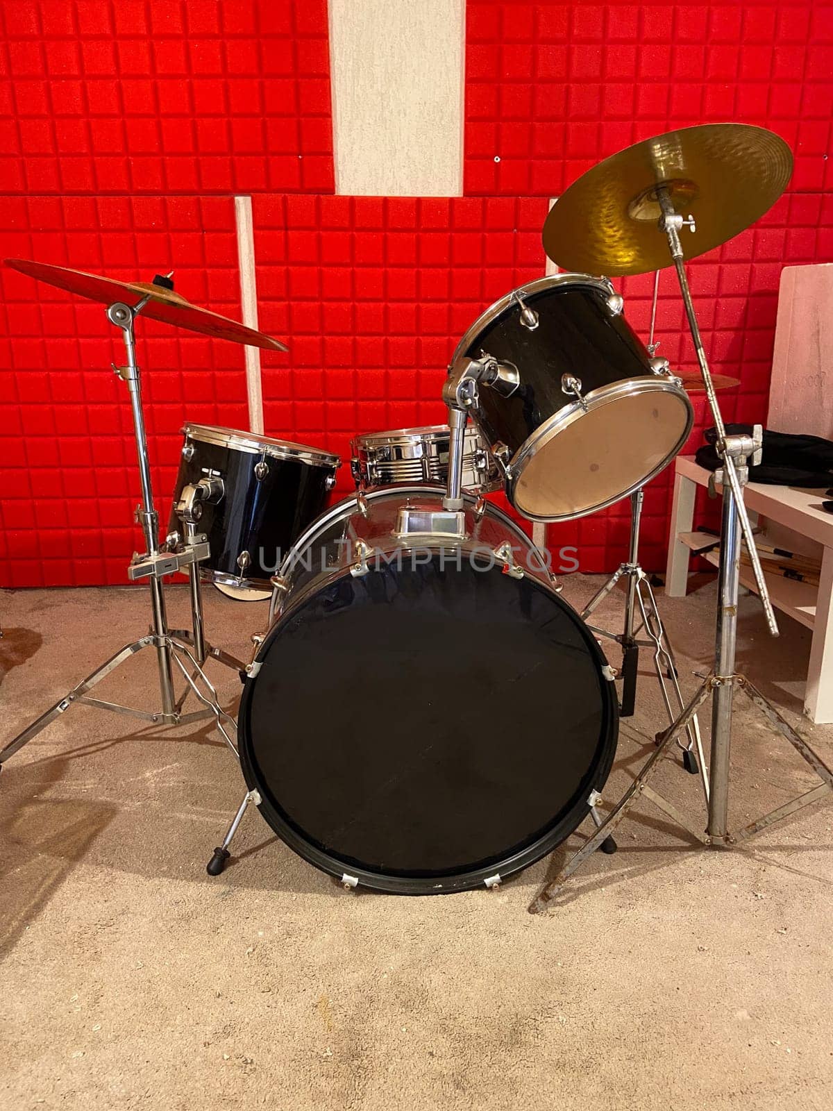Classic black drum set is positioned in a studio with vibrant red soundproof walls. Shiny black drums and bright red background creates a dynamic and energetic music atmosphere. Musical instrument and creative art concept.