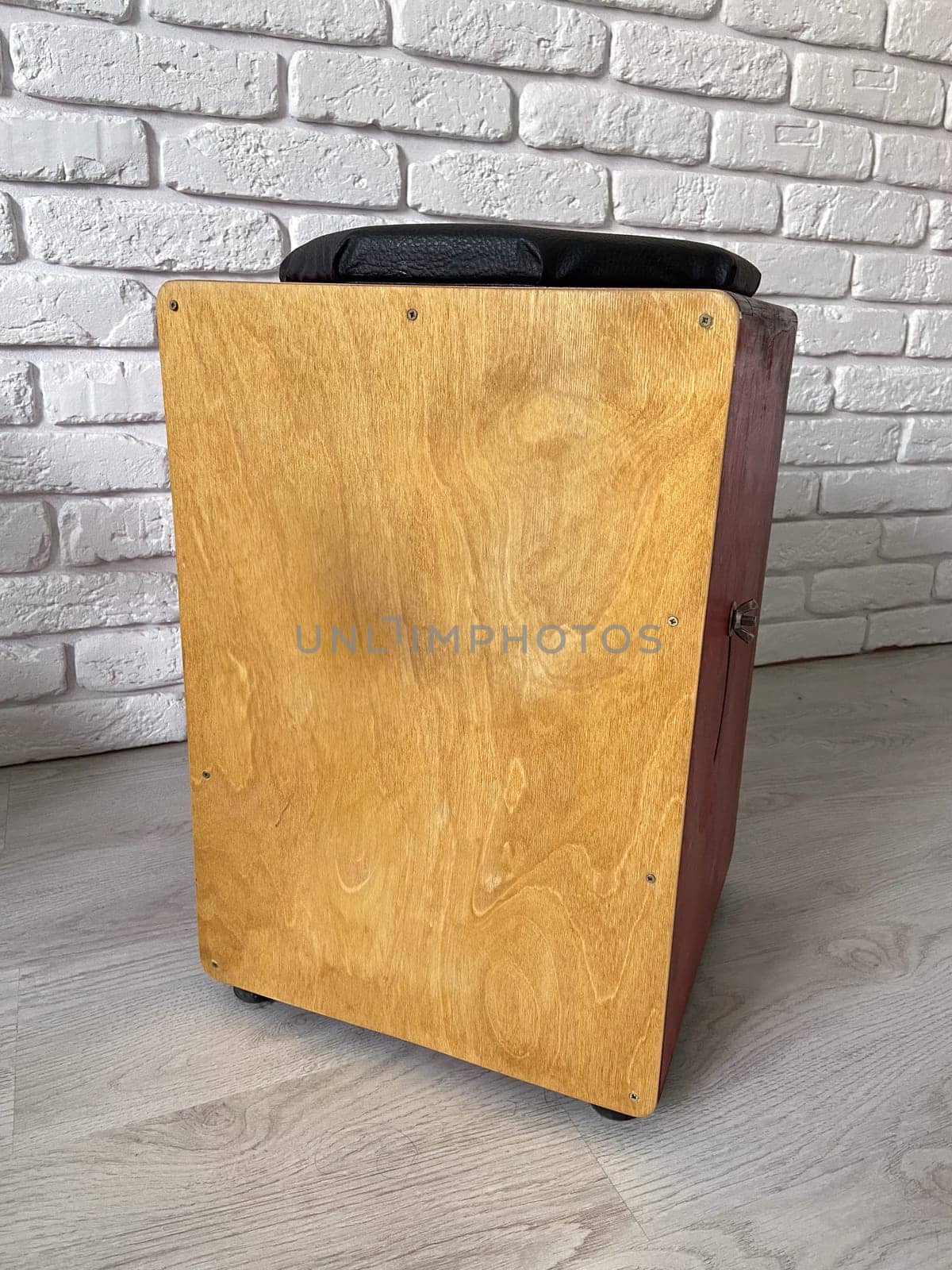 Cajon drum sits elegantly against a textured white brick wall, highlighting its wooden craftsmanship. Musical Instrument for creating music at home and hobby concept.