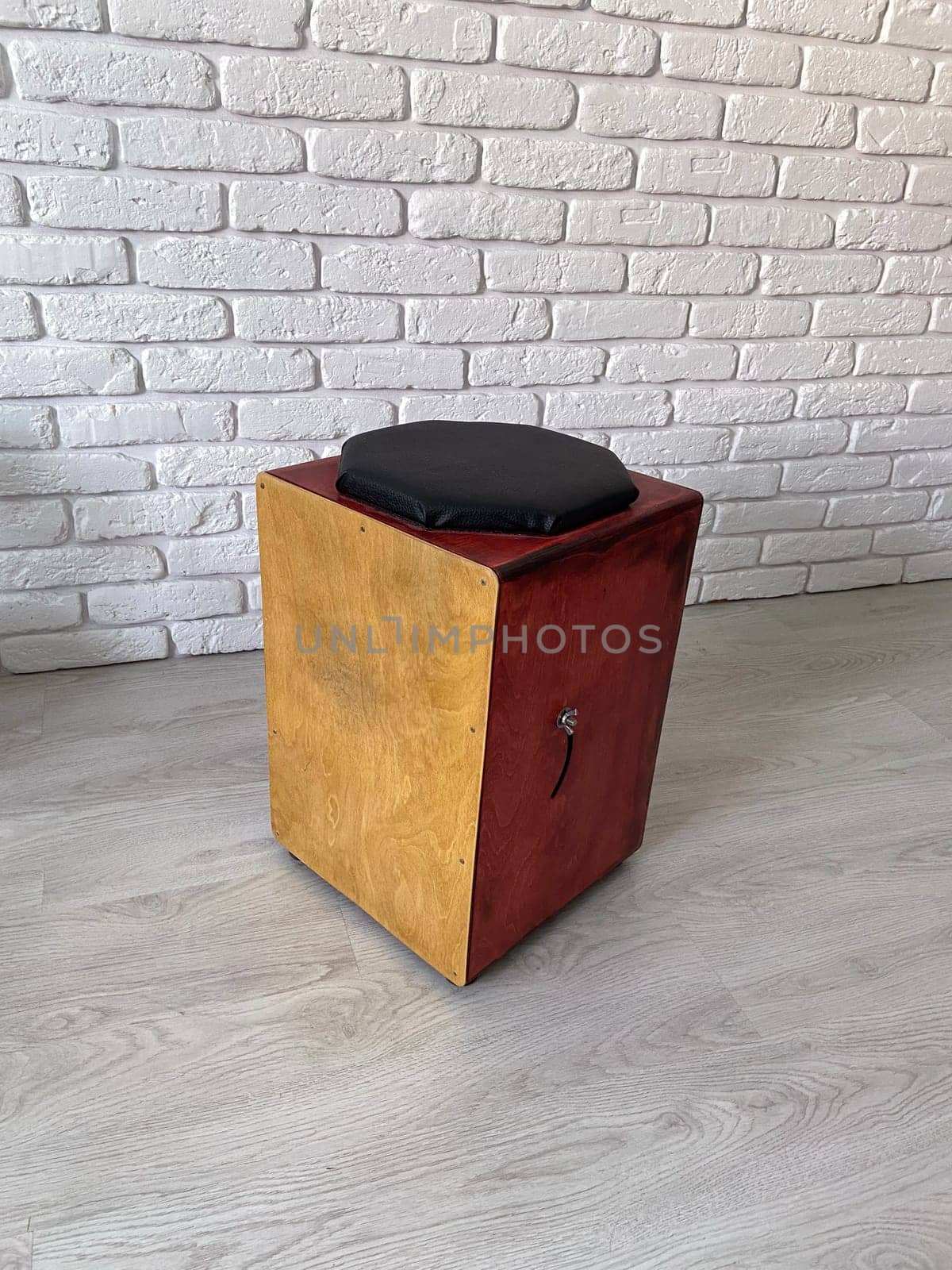 Cajon drum sits elegantly against a textured white brick wall, highlighting its wooden craftsmanship. Musical Instrument for creating music at home and hobby concept.