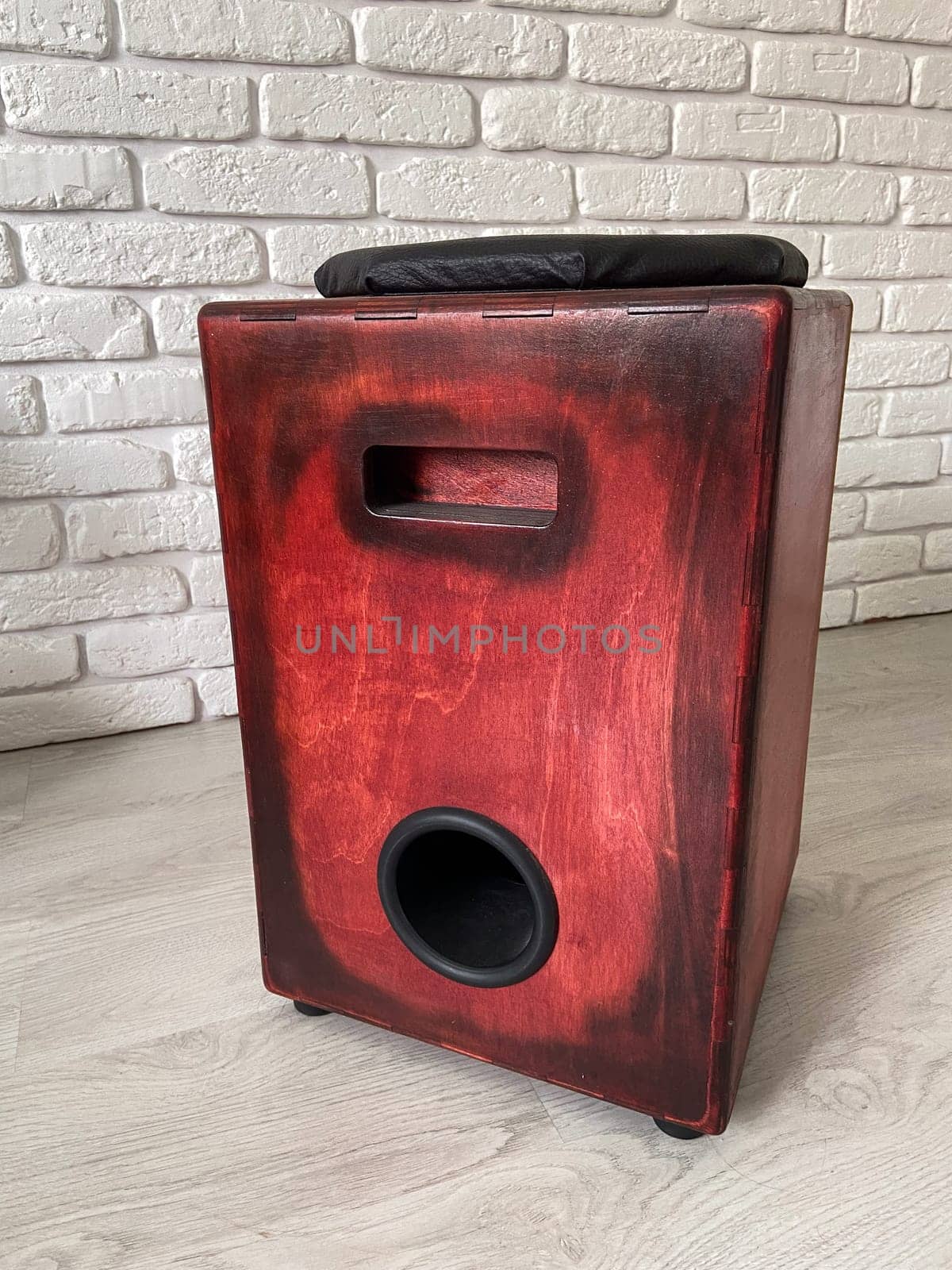 Cajon drum sits elegantly against a textured white brick wall, highlighting its wooden craftsmanship. Musical Instrument for creating music at home and hobby concept.