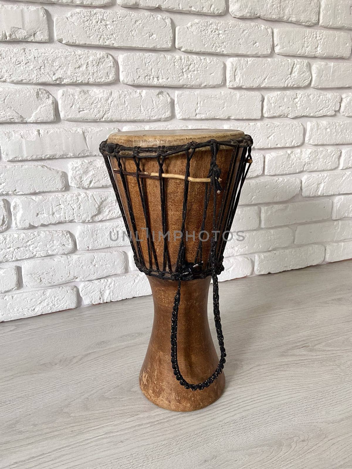 Traditional djembe drum stands in front of a textured white brick wall. Musical instrument and ethnic music concept.