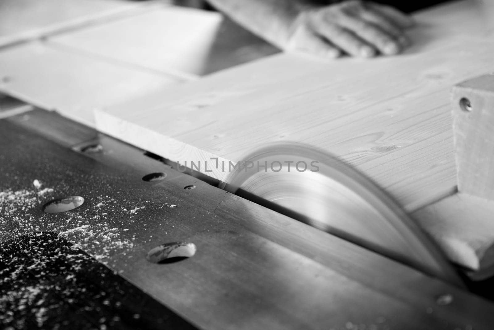 Skilled carpenter cutting wooden plank with circular saw in cozy workshop, creating sawdust. Close up captures labor intensive woodworking process. - black n white -
