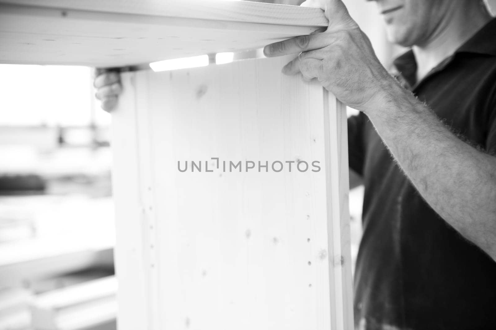 Carpenter is assembling a piece of wooden furniture in his workshop, his experienced hands carefully aligning the pieces. - black n white -