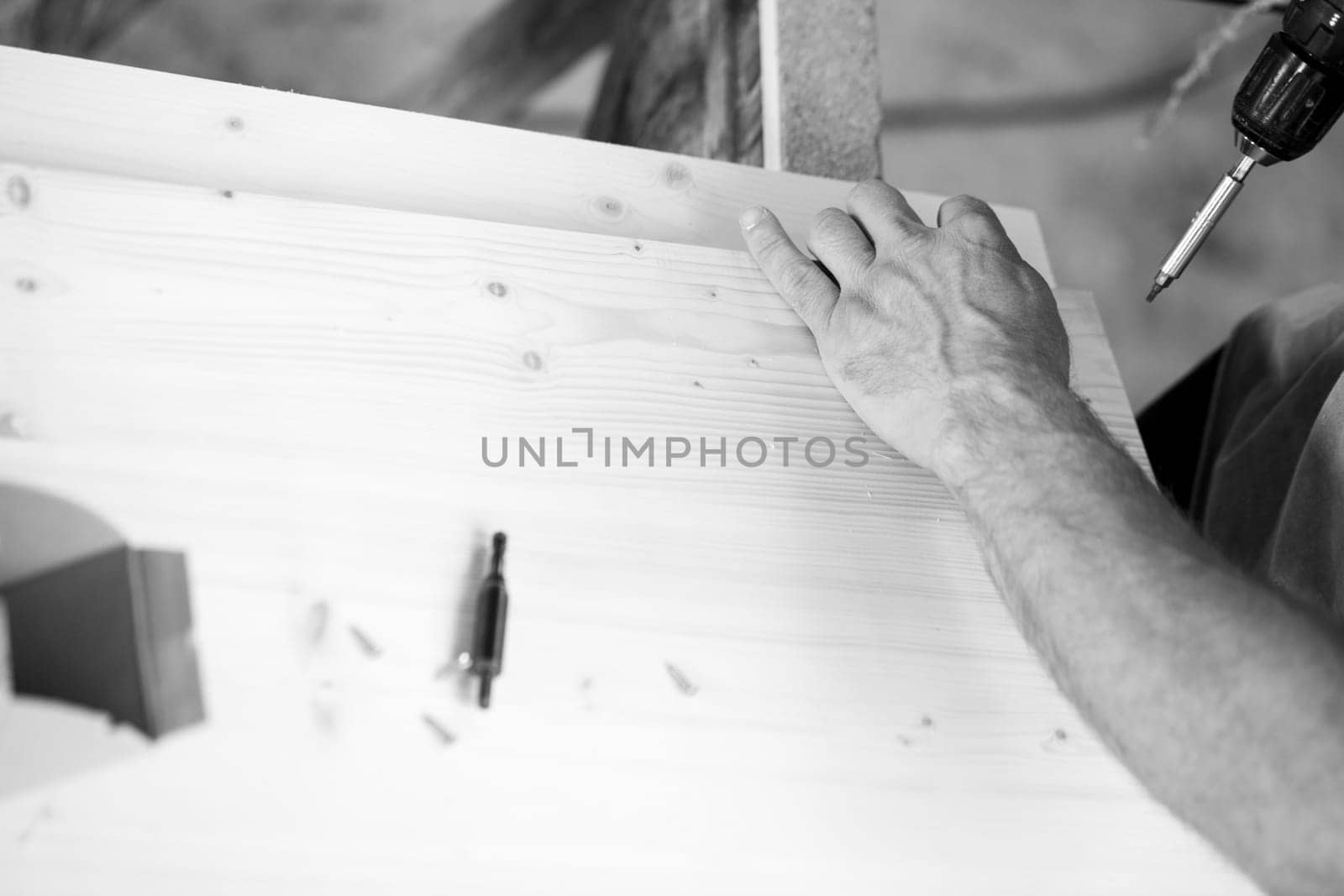 Carpenter inspects a wooden plank in a workshop, surrounded by sawdust and tools. - black n white -