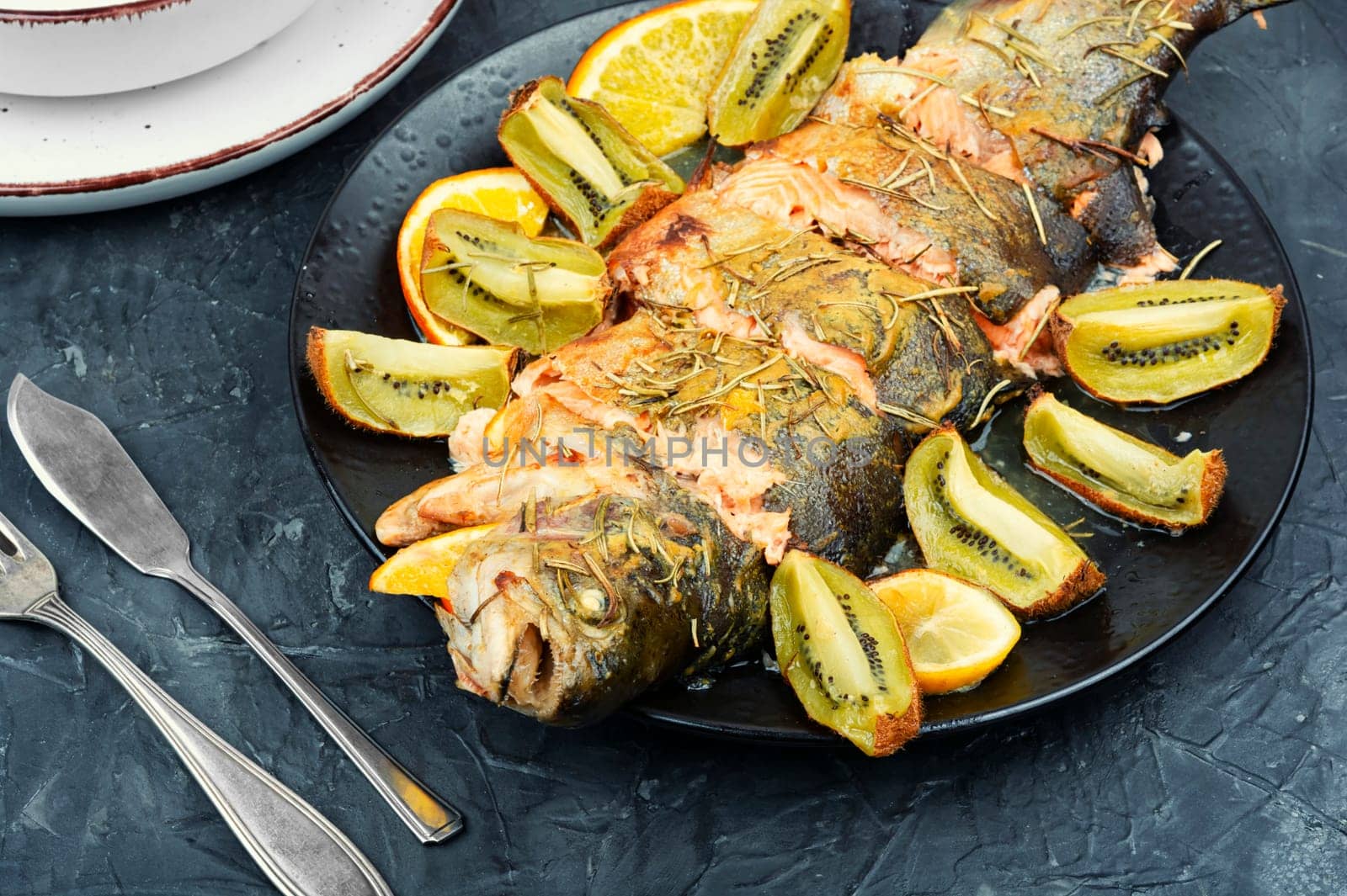 Plate of whole baked trout, served with kiwi fruit and orange.