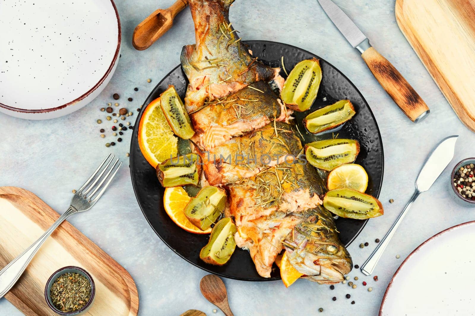 Plate of whole baked trout, served with kiwi fruit and orange.