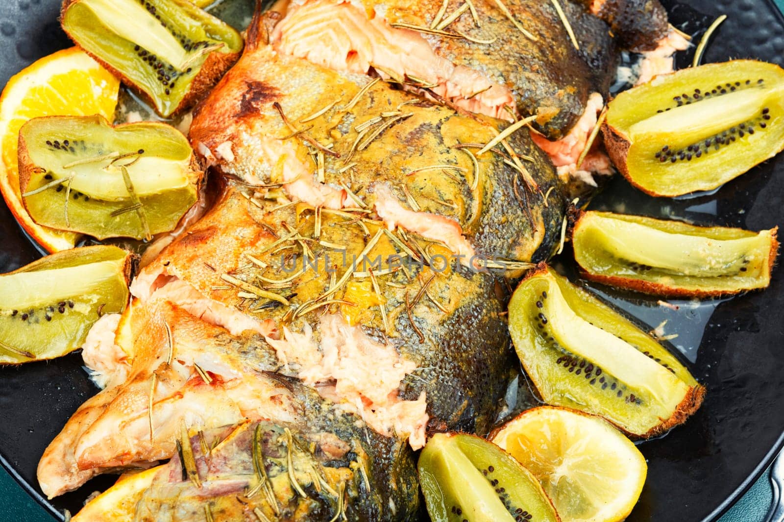 Plate of whole baked trout, served with kiwi fruit and orange.