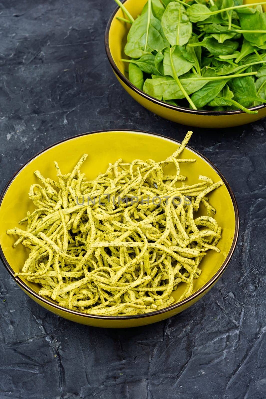 Uncooked spinach pasta tagliatelle with fresh spinach leaves.